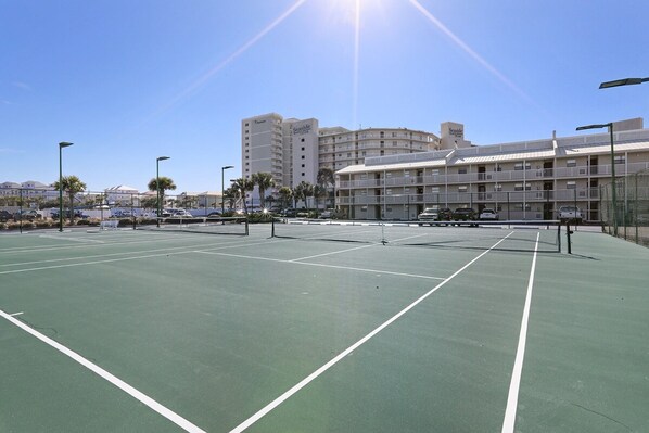 An outdoor tennis court with a net, surrounded by a fence and palm trees. - Seaside Beach 5417- Two Bedrooms Waterfront Condo With Pool Sauna Amazing Ocean View Balcony (Orange Beach)