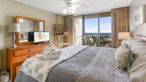 A hotel room with a bed, a television, a ceiling fan, a large window with a view of the ocean, and a balcony. - Seaside Beach 5417- Two Bedrooms Waterfront Condo With Pool Sauna Amazing Ocean View Balcony (Orange Beach)