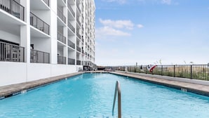 Une piscine entourée d’une rambarde métallique, située à côté d’un bâtiment blanc doté de balcons.