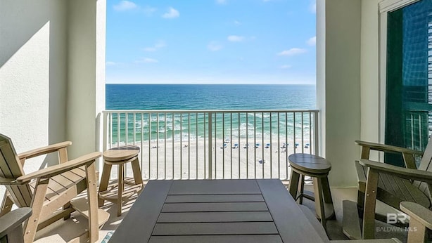 A balcony with a view of the ocean, wooden chairs, and a table. - Regency Isle 1102 3 3 2 Covered Parking Spots Penthouse (Orange Beach)