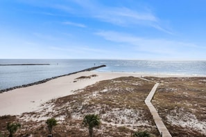 Una playa con un paseo marítimo de madera, dunas arenosas y un rompeolas rocoso.