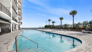 A swimming pool with a metal ladder, surrounded by lounge chairs and palm trees, adjacent to a multi-story building. - Grand Pointe 512 Gulf-front Stunning Views Top-notch Amenities (Orange Beach)