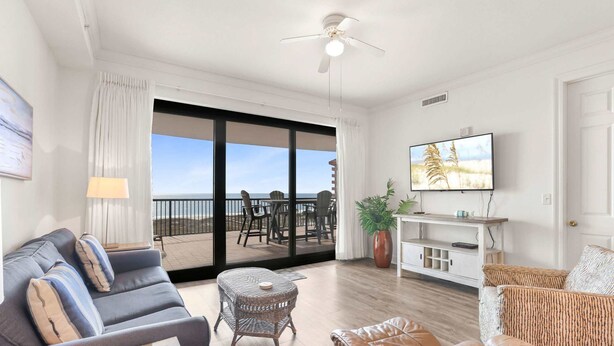 A spacious living area with a balcony, a sofa, a coffee table, a TV, and a plant. - Grand Pointe 512 Gulf-front Stunning Views Top-notch Amenities (Orange Beach)