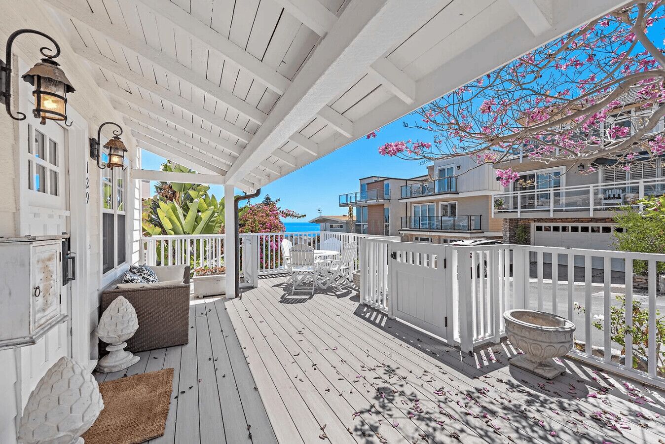 A covered outdoor deck with white railings, wicker furniture, and a view of the ocean.