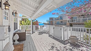A covered outdoor deck with white railings, wicker furniture, and a view of the ocean. - Luxurious Seaside Escape-85 Steps to the Beach-Panoramic Ocean Views (Laguna Beach)