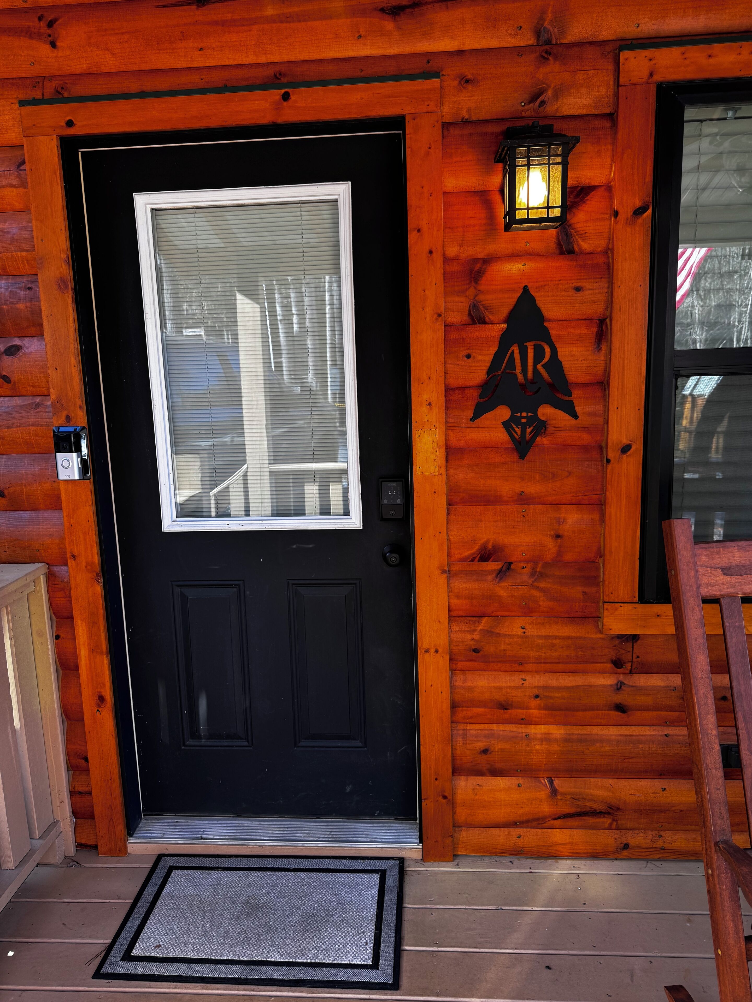 A black door with a window, a wooden wall with a logo, and a wooden chair.