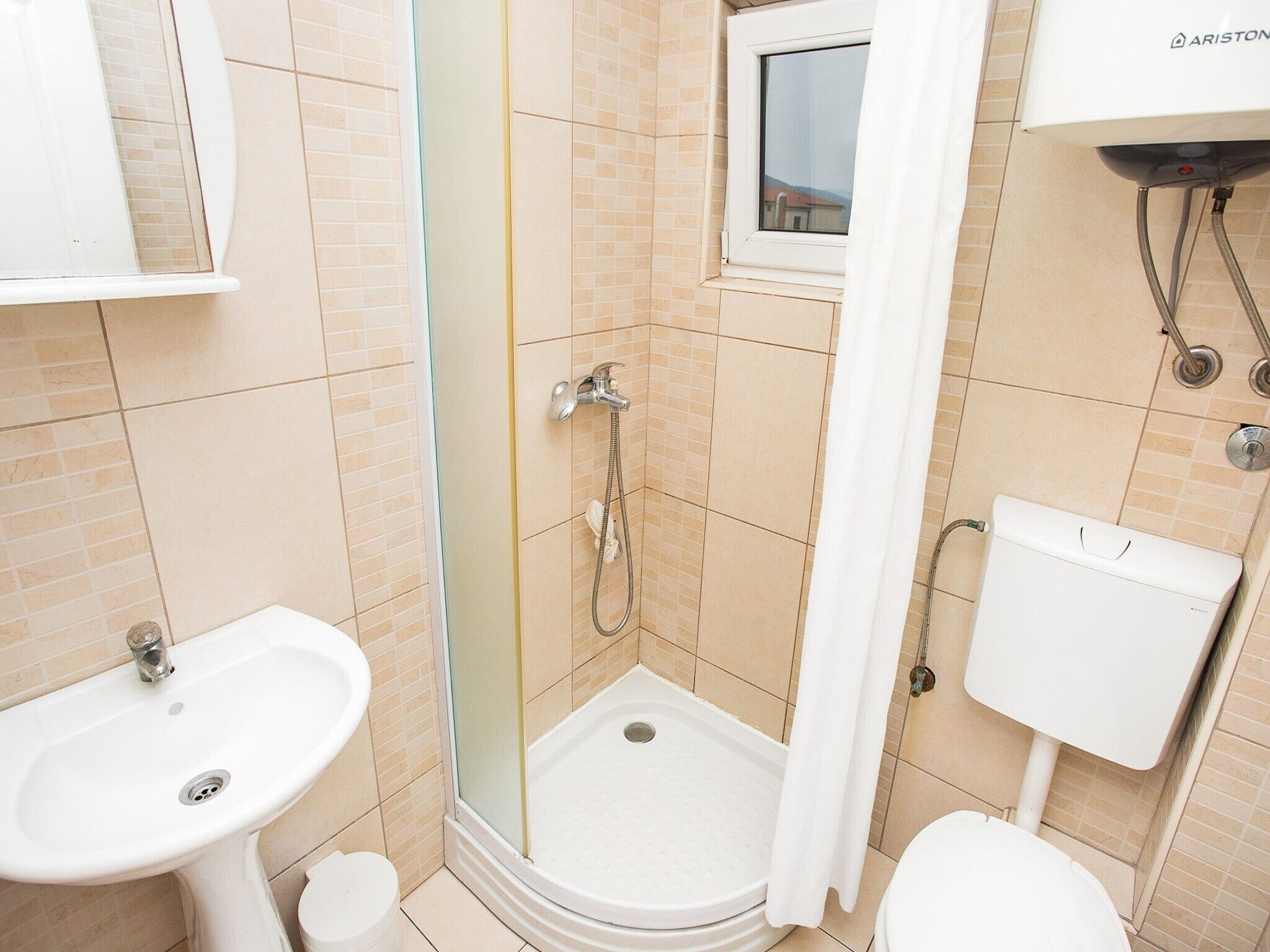 Un baño con ducha, lavabo, inodoro y ventana.