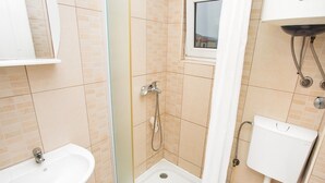 Et badeværelse med bruser, vask, toilet og et vindue.