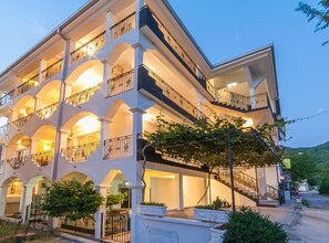 Un hotel de varios pisos con balcones, mobiliario exterior y un jardín ajardinado.