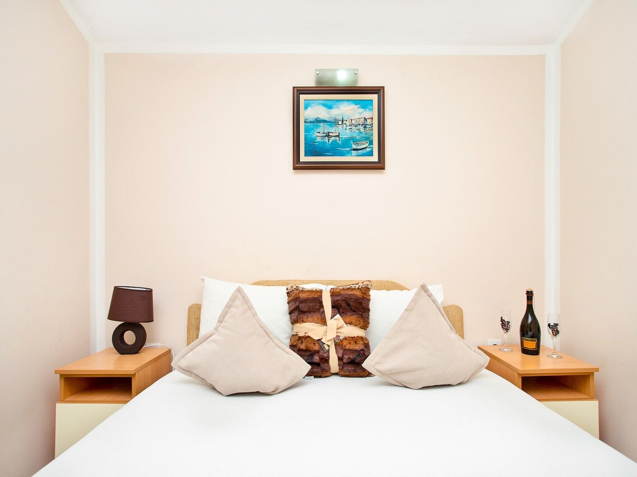 Habitación de hotel con cama, dos mesitas de noche, una lámpara, una botella de vino y un cuadro en la pared.