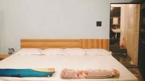 A hotel room with a wooden headboard, a bed with white linens, a blue and yellow pillow, and a floral blanket. - Shreeram guest house (Ujjain)