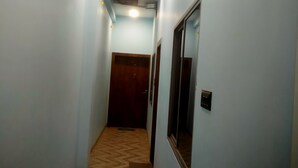 A narrow hallway with light blue walls, a wooden floor, and a door at the end. - Shreeram guest house (Ujjain)