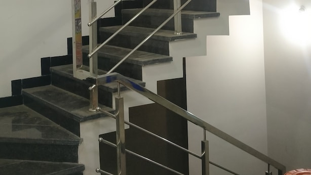A modern staircase with metal railings and dark steps, leading to a landing with a light fixture. - Shreeram guest house (Ujjain)