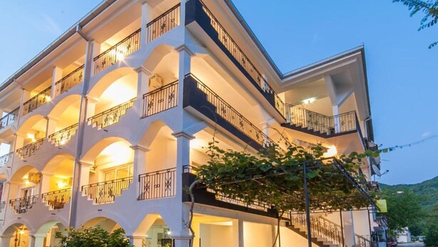 Een meerlaags hotel met balkons, buiten zitplaatsen en een aangelegde tuin.