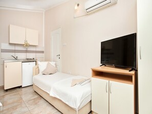 Ein kleines Hotelzimmer mit Küchenzeile, einem Bett mit weißer Bettwäsche, einem Fernseher auf einem Holzboden und einem Kleiderschrank.