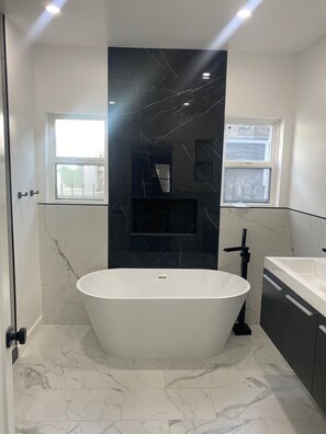 Ein modernes Badezimmer mit einer freistehenden Badewanne, Marmorwänden und einem Fenster, das für natürliches Licht sorgt.