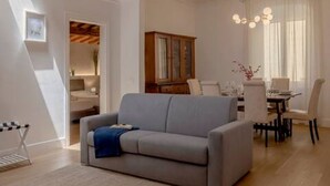 A modern living room with a grey sofa, a dining area with a table and chairs, and a wooden cabinet.