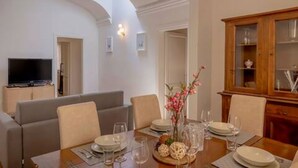 A dining area with a table set for four, a television in the background, and a wooden cabinet with glass doors.