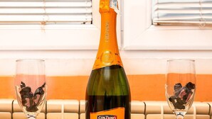 A bottle of Cinzano Prosecco D.O.C. on a table with two glasses containing chocolate pieces.