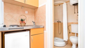 A compact kitchen with a refrigerator, a sink, and a basket of fruit.