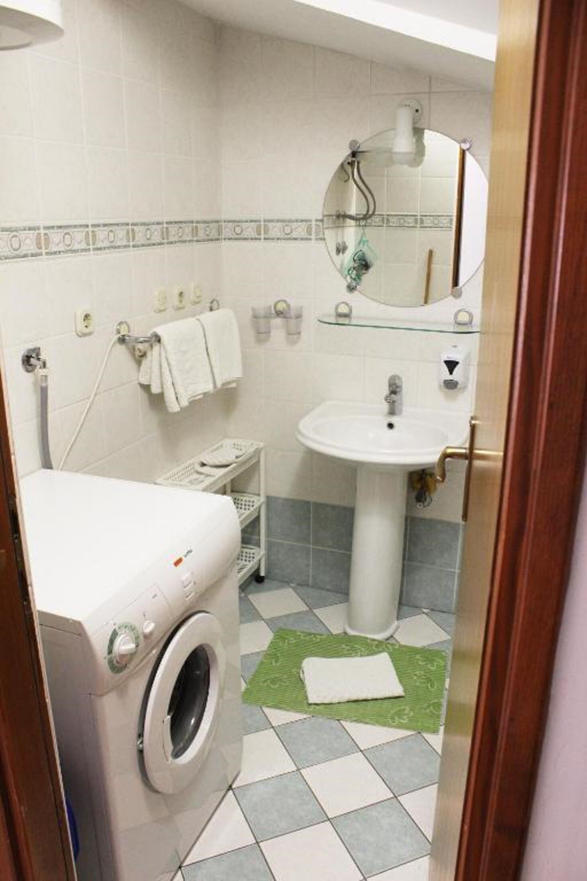A compact bathroom with a washing machine, a sink, and a mirror.