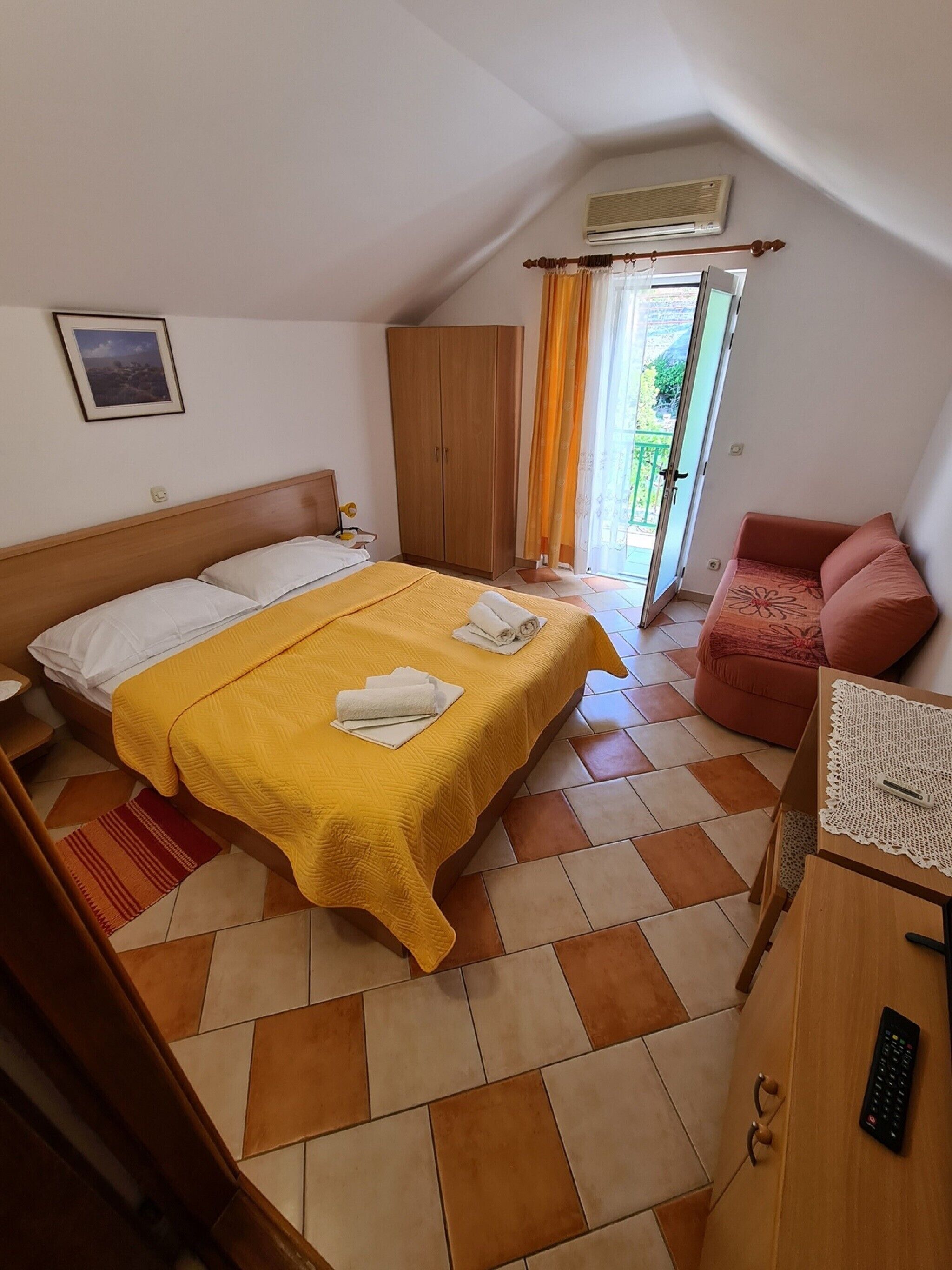 A bedroom with a bed, a wardrobe, a sofa, and a desk with a remote control.