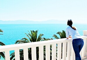A woman standing on a balcony overlooking a body of water with palm trees and distant mountains. - Apartments Pansion Franka 3* - Apartment 12 (Brist)