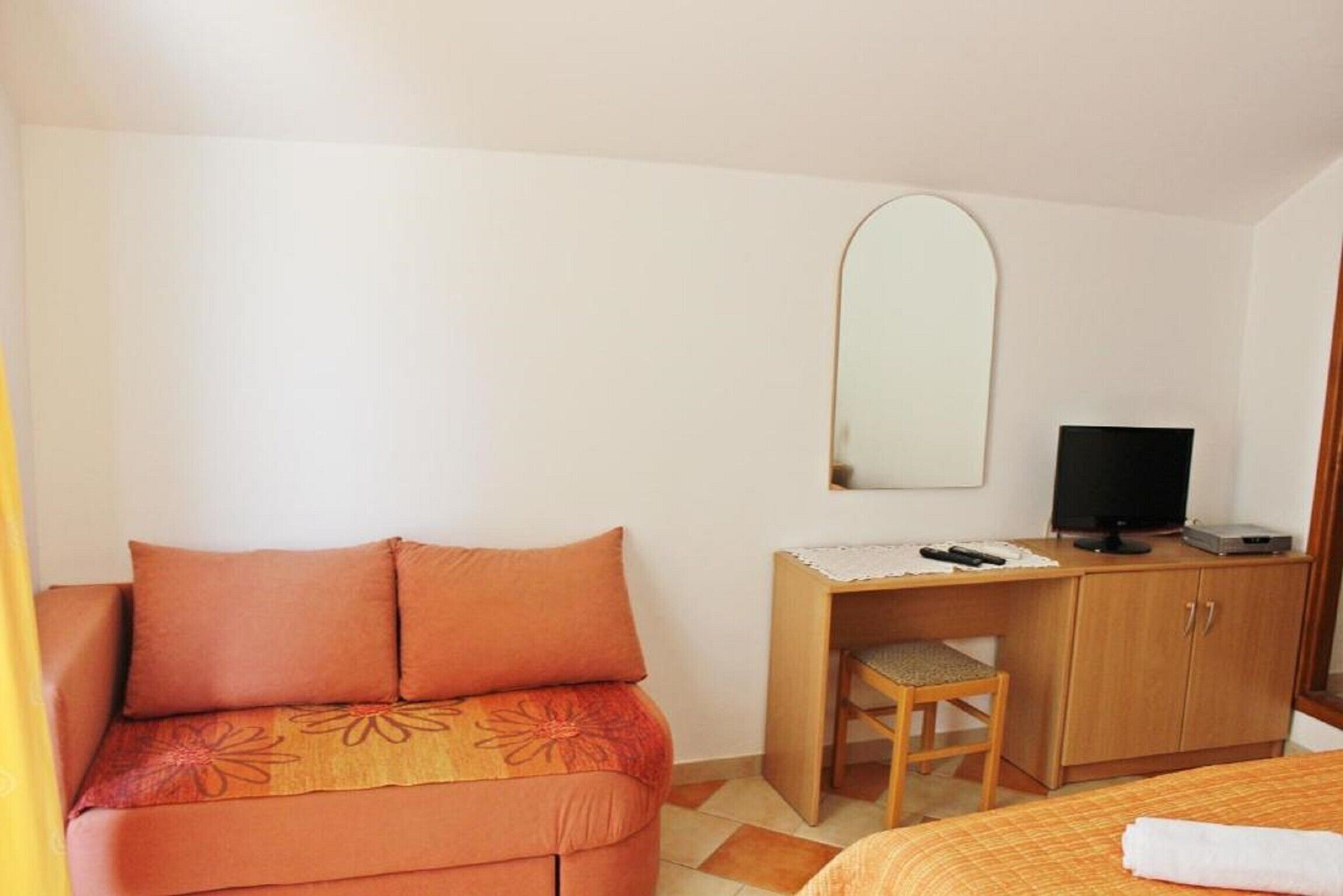 A bedroom with a bed, a desk with a chair, a television, and a wardrobe.