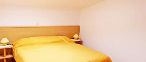 A room with a bed, two bedside tables with lamps, a skylight, and a tiled floor.