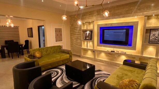 A modern living room with a green sofa, black coffee table, and a flat-screen TV mounted on the wall. - Spacious 3-bedroom apartment in excellent Abuja with AC, WiFi, fitness room (Abuja)