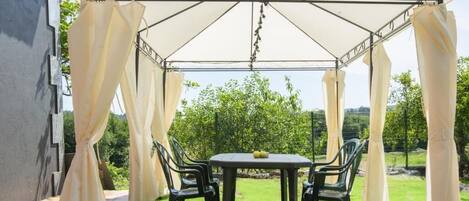 Un patio cubierto con mesa y sillas, rodeado de cortinas blancas.