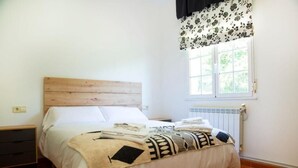 A bedroom with a wooden headboard, white bedding, a window with a floral valance, and a radiator.
