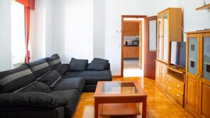 A living room with a dark-colored sofa, a glass-top coffee table, and wooden cabinets with a television.
