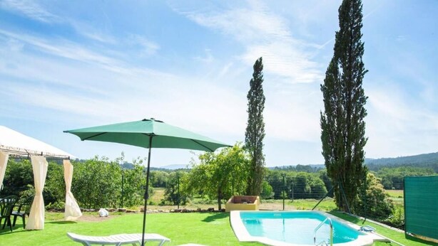 A backyard with a swimming pool, a lounge chair, and a pergola with a green umbrella.