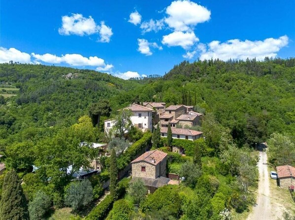 A hillside village with traditional stone buildings, a dirt path, and lush greenery.