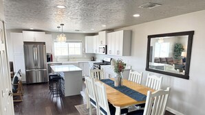 Une cuisine moderne avec des meubles blancs, un réfrigérateur en acier inoxydable, un îlot central doté de sièges et une table à manger avec des chaises.