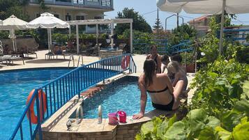 Zona de piscina con escalones de acceso, sillones reclinables y sombrillas.