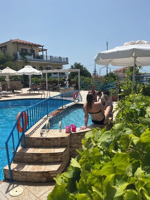 Area piscina con scalini che conducono all'acqua, sedie a sdraio e ombrelloni.
