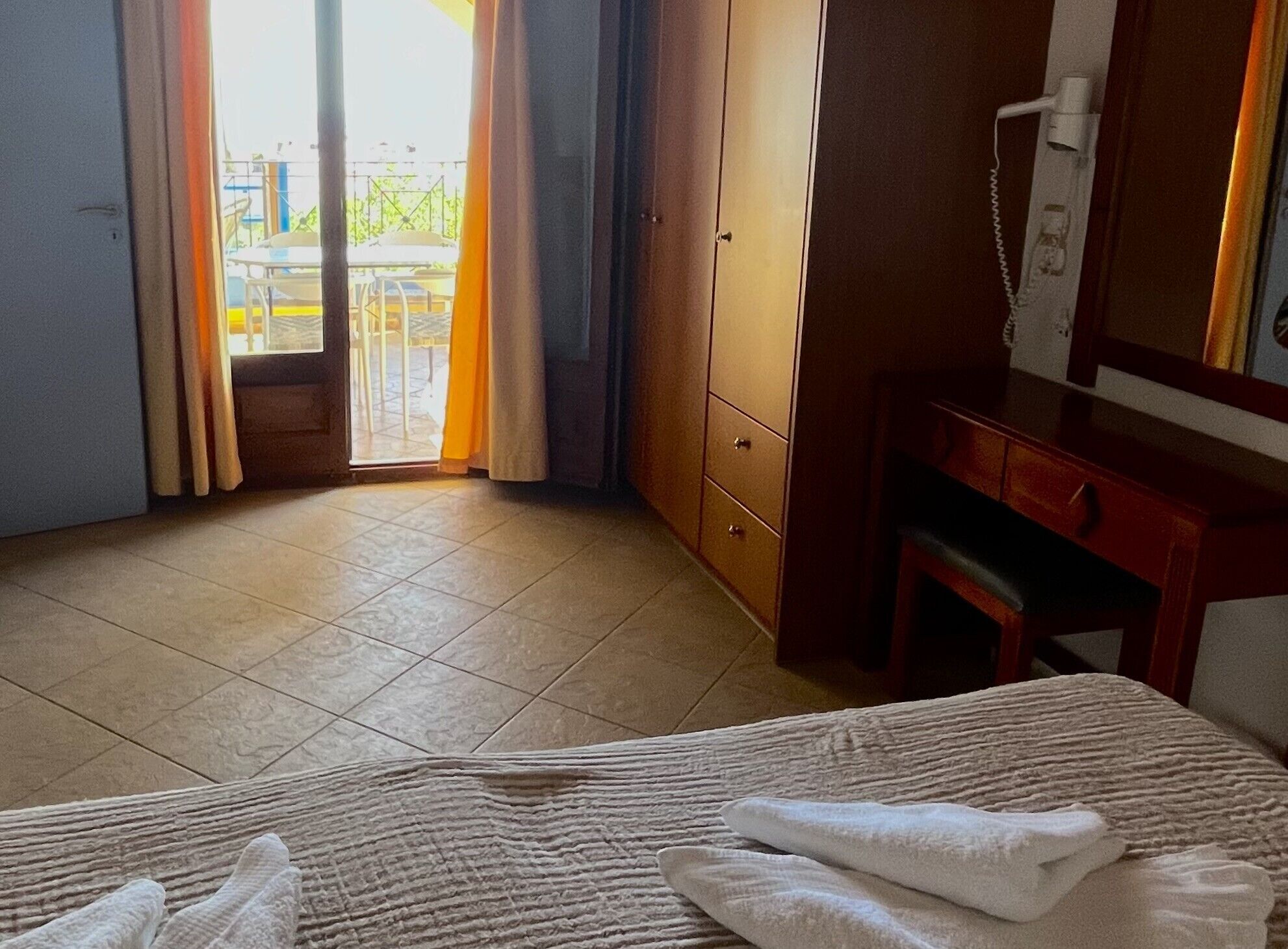 A hotel room with a bed, a desk, a telephone, and a view of the outside balcony.