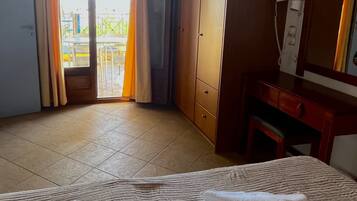 A hotel room with a bed, a desk, a telephone, and a view of the outside balcony.