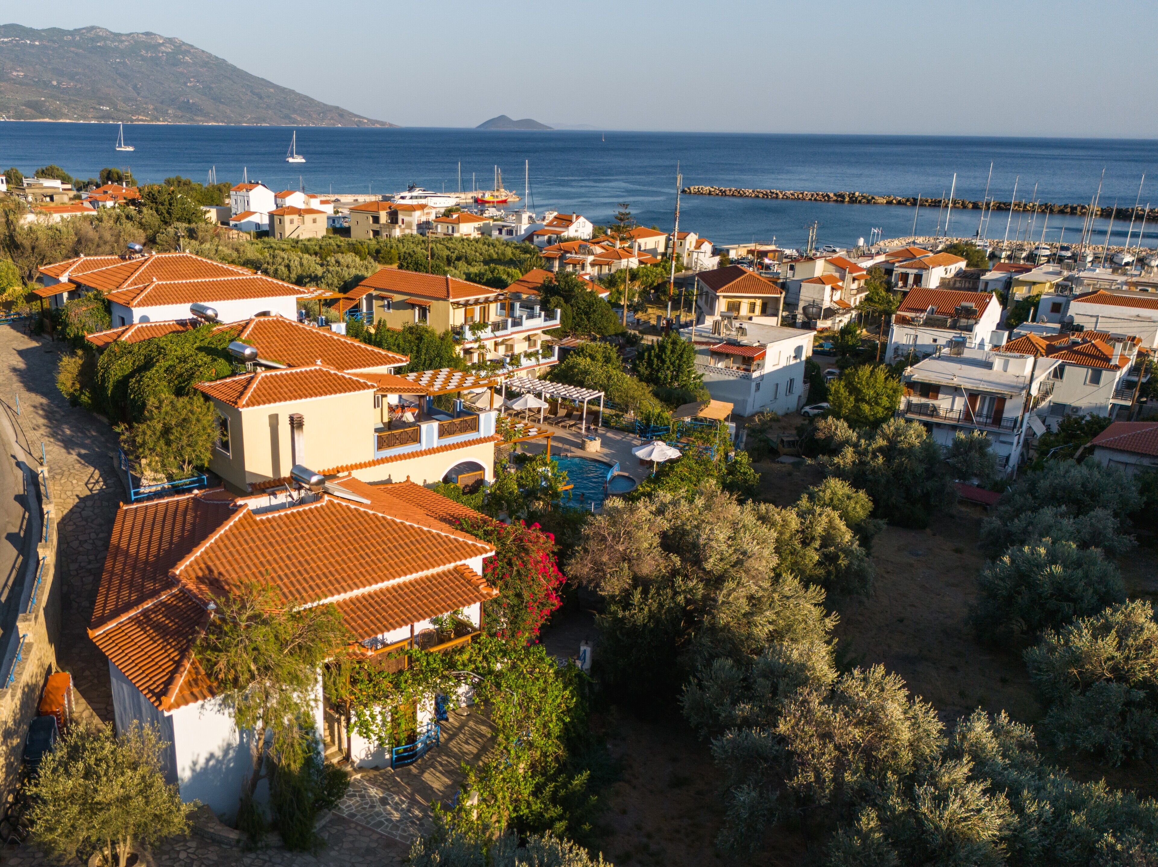 A coastal residential area with houses featuring red-tiled roofs, a swimming pool, and a view of the sea.
