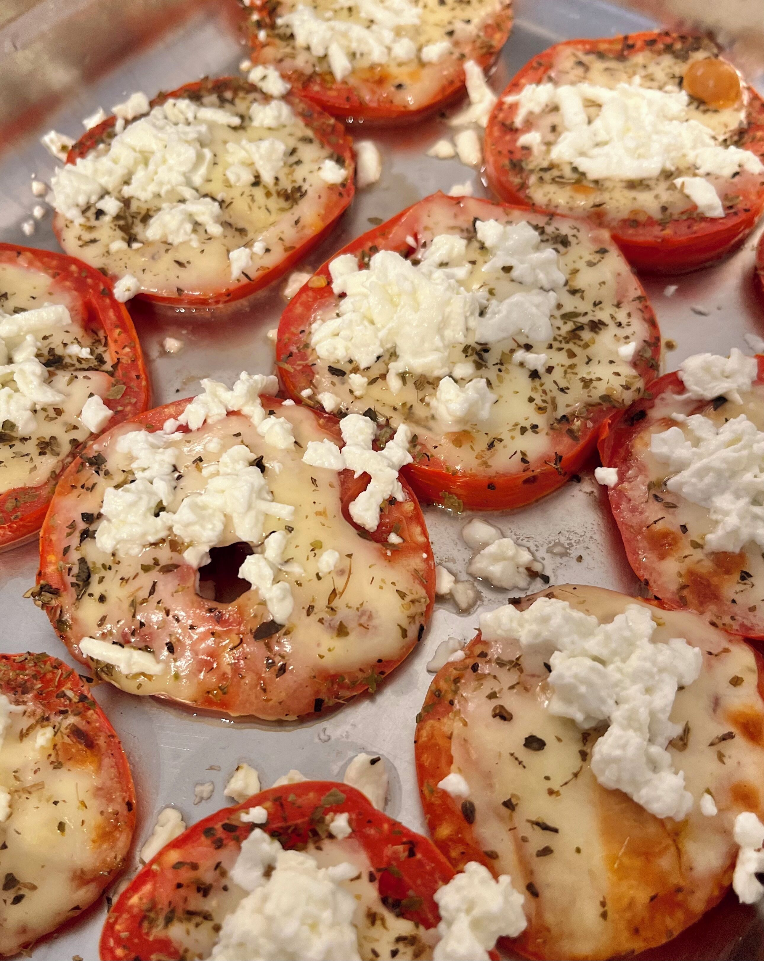 Una bandeja de tomates al horno cubiertos con queso y hierbas.