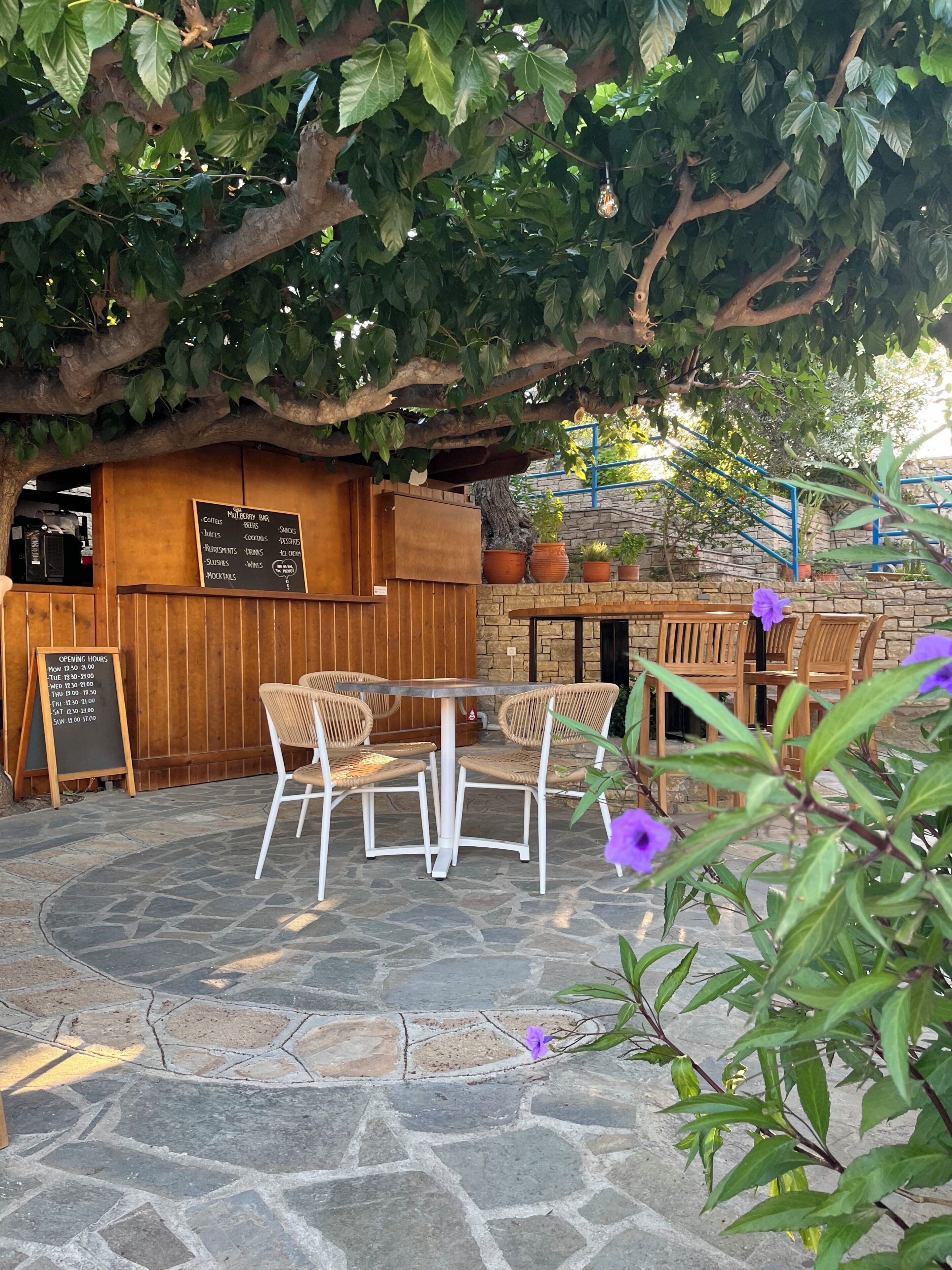 An outdoor seating area with stone flooring, wooden tables, and chairs.