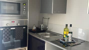 Eine kleine Küche mit Mikrowelle, Herd und Spüle. Im Schrank befinden sich Möbel, eine Kaffeemaschine und eine Flasche Olivenöl.