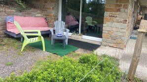 A stone building with a glass door leading to an outdoor seating area with a green lawn, a white chair, and a sofa with a pink cover. - Studio in a country home (Cordemais)