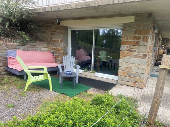 A stone building with a glass door leading to an outdoor seating area with a green lawn, a white chair, and a sofa with a pink cover. - Private studio in the countryside, located in a local resident's home (Cordemais)