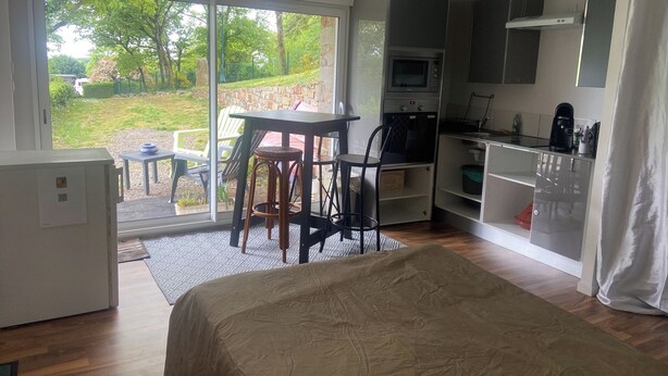 A modern room with a bed, a dining table, a kitchen area, and a sliding glass door leading to a garden. - Studio in a country home (Cordemais)