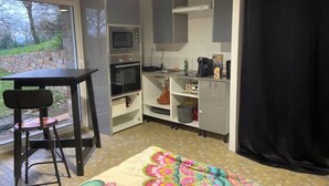 A compact kitchen with a microwave, oven, and coffee maker, a small dining area with a table and chairs, and a view of the outdoors through a window. - Studio in a country home (Cordemais)
