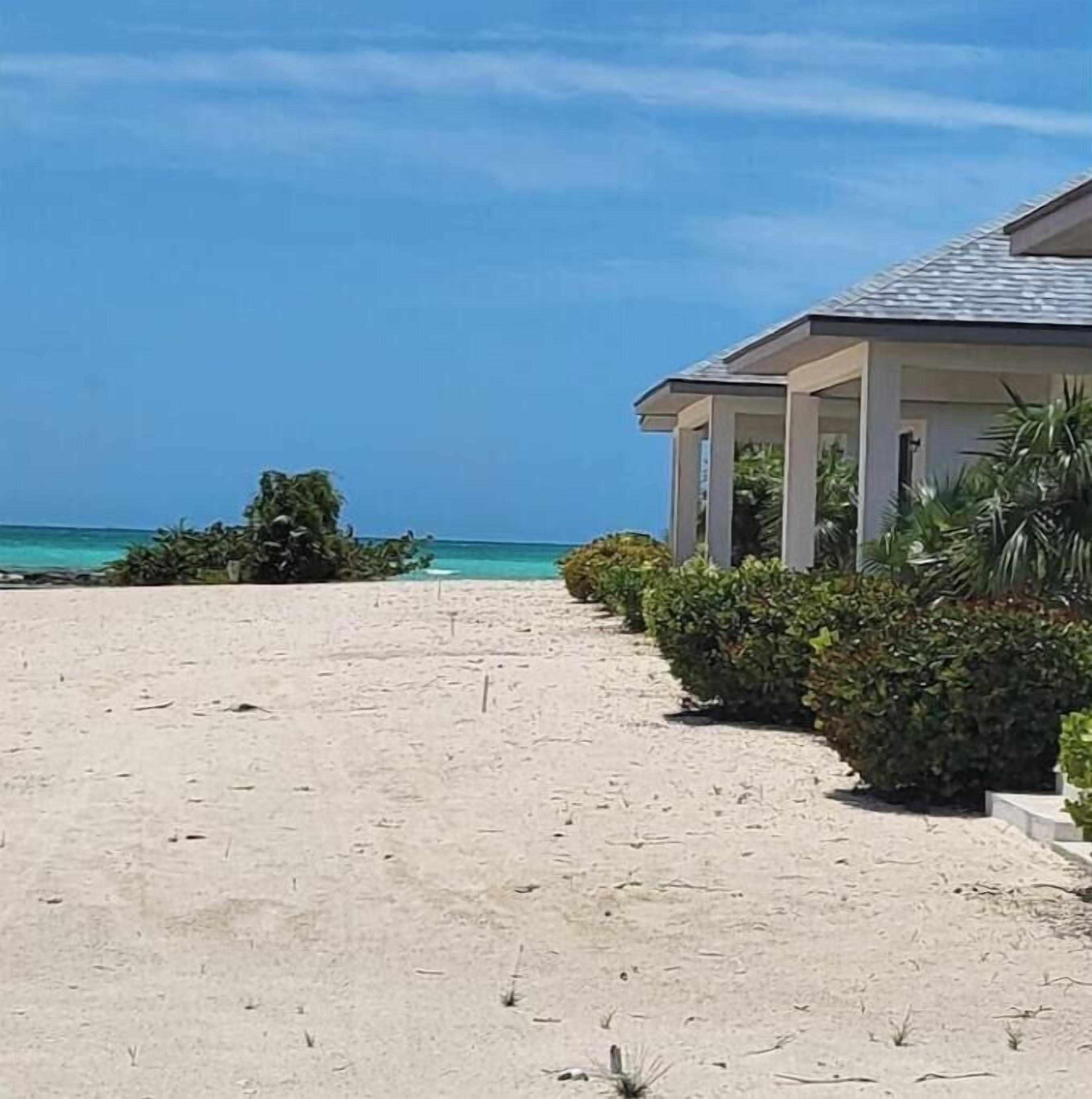 A beachfront property with a covered walkway leading to a building, surrounded by sand and vegetation.