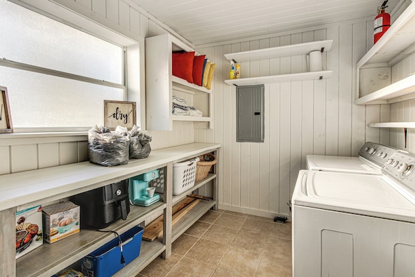 A laundry room with a washing machine, shelves with towels and laundry supplies, and a window with a view. - Tranquil Gantt Lake Home w/ Deck & Patio! (Andalusia)